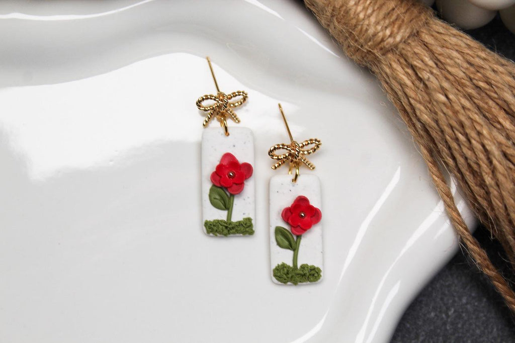 Pair of earrings with red floral designs on a white dish.