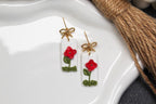Pair of earrings with red floral designs on a white dish.