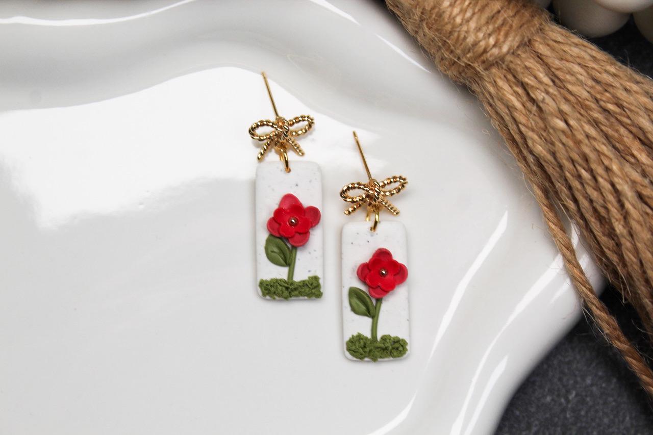 Pair of earrings with red floral designs on a white dish.