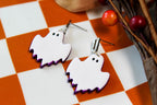 Ghost-shaped earrings on a checkered surface with decorative elements.