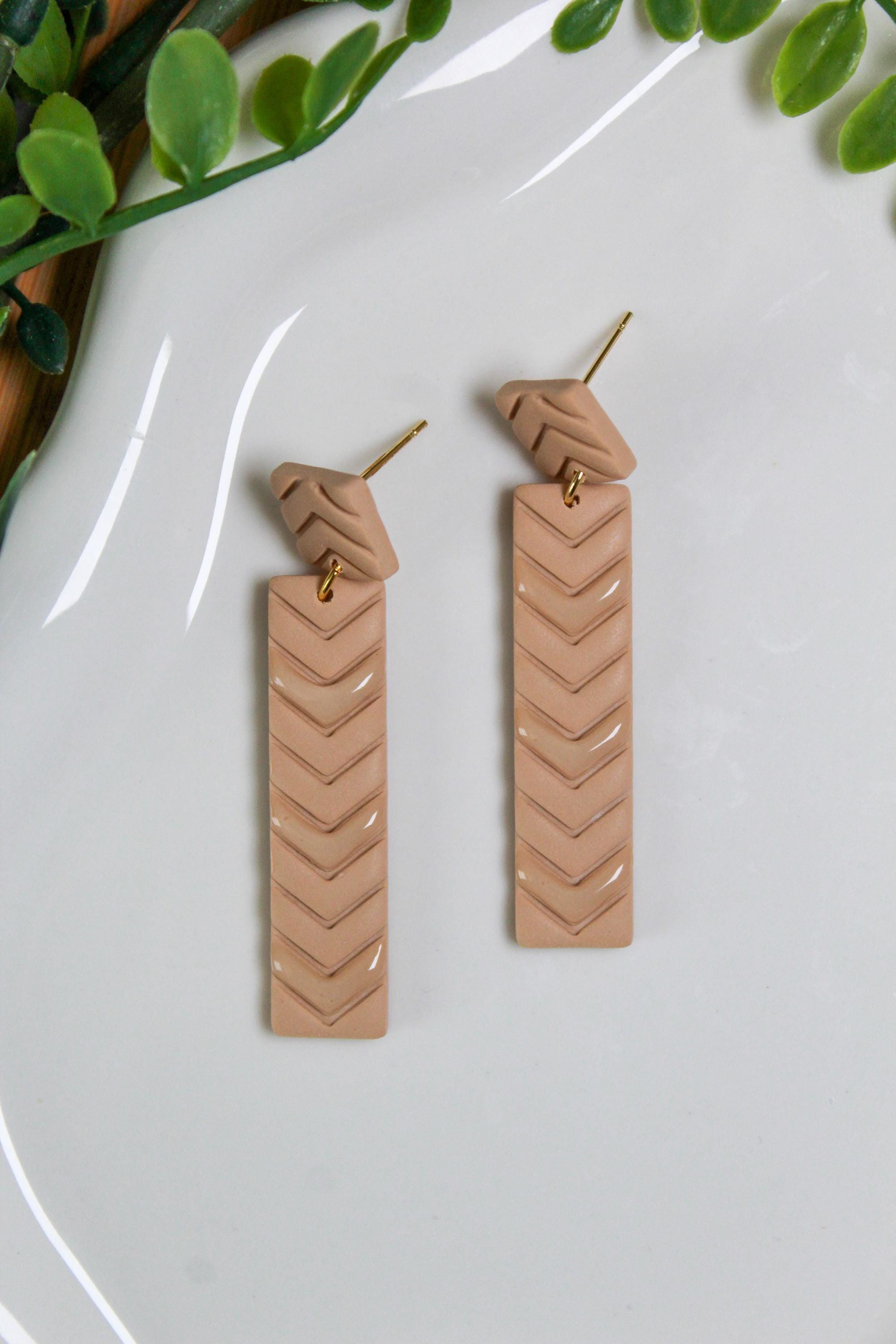 Pair of tan chevron patterned earrings on a white plate with green leaves in the background