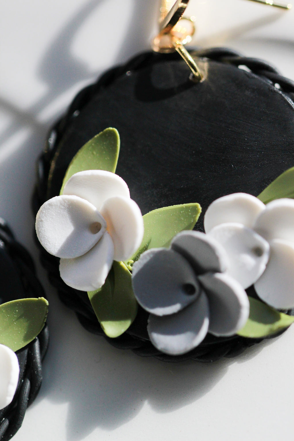 Black circular earrings with white and gray floral designs on a light background