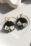 Black floral earrings with gold hooks on a white surface