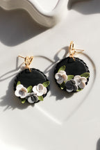 Black floral earrings with gold hooks on a white surface
