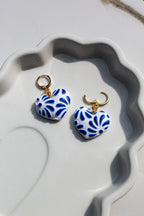 Heart-shaped blue and white earrings with gold hooks on a textured white surface.