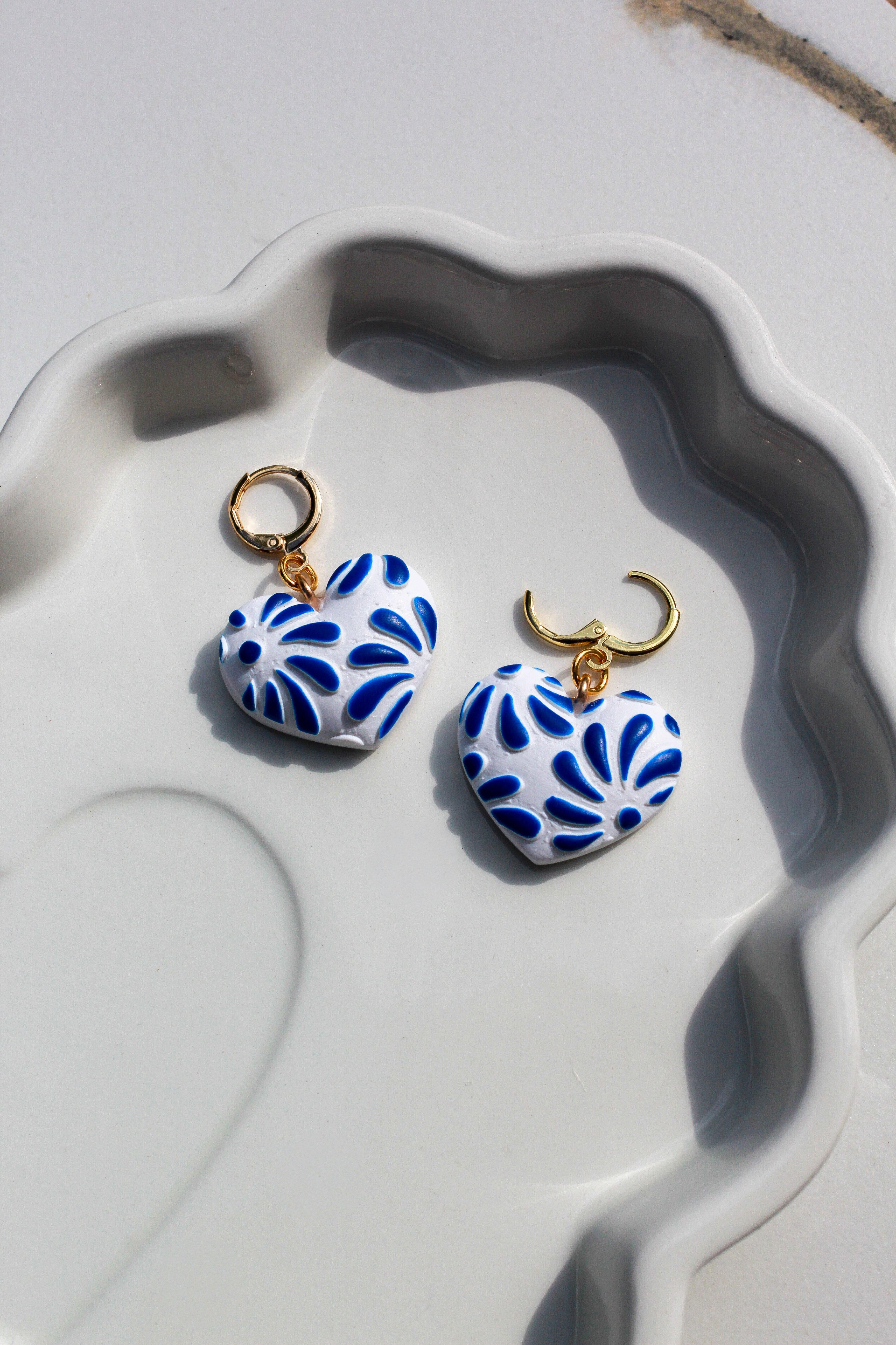Heart-shaped blue and white earrings with gold hooks on a textured white surface.
