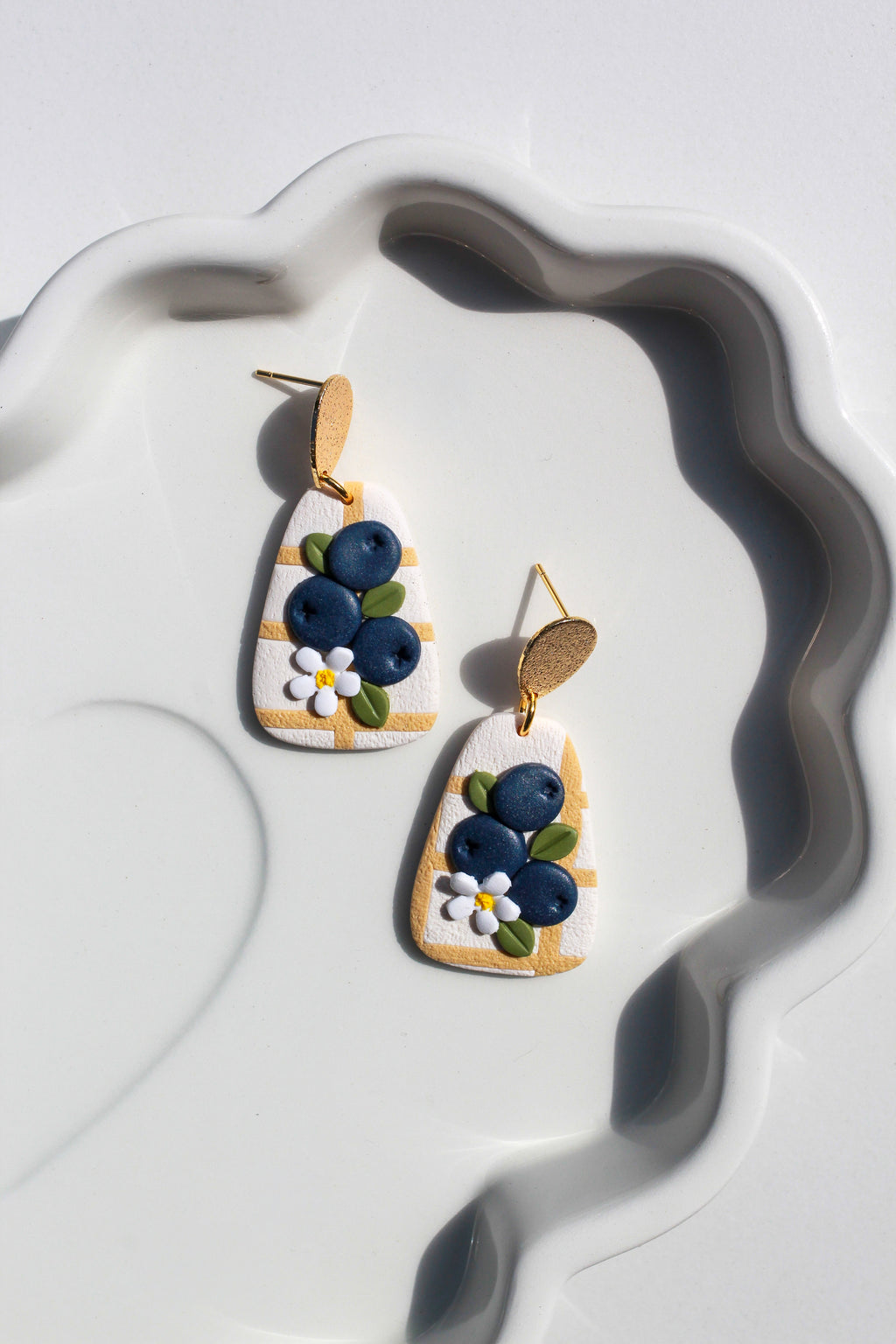 Pair of earrings with blueberry design on a white dish