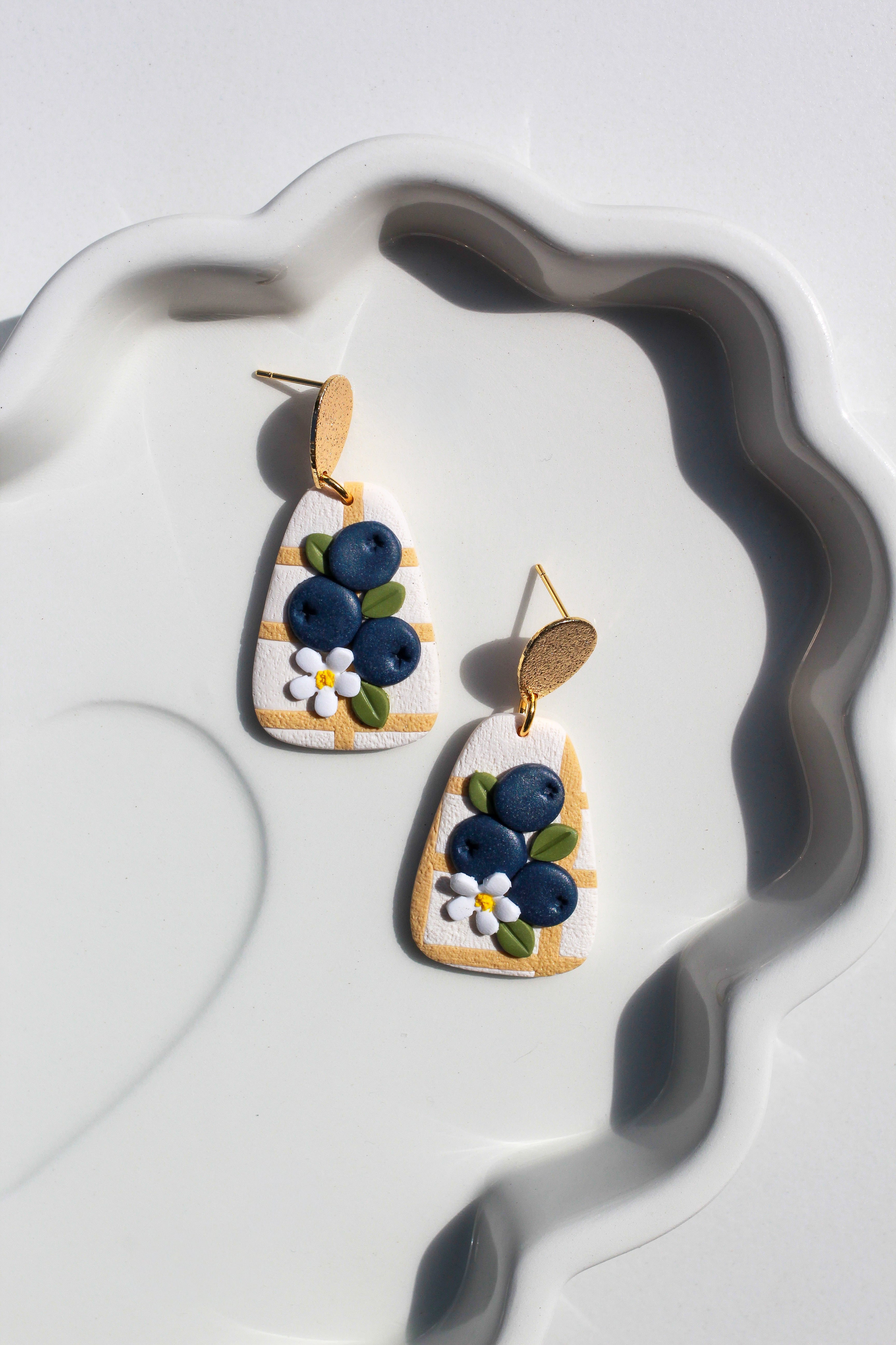 Pair of earrings with blueberry design on a white dish
