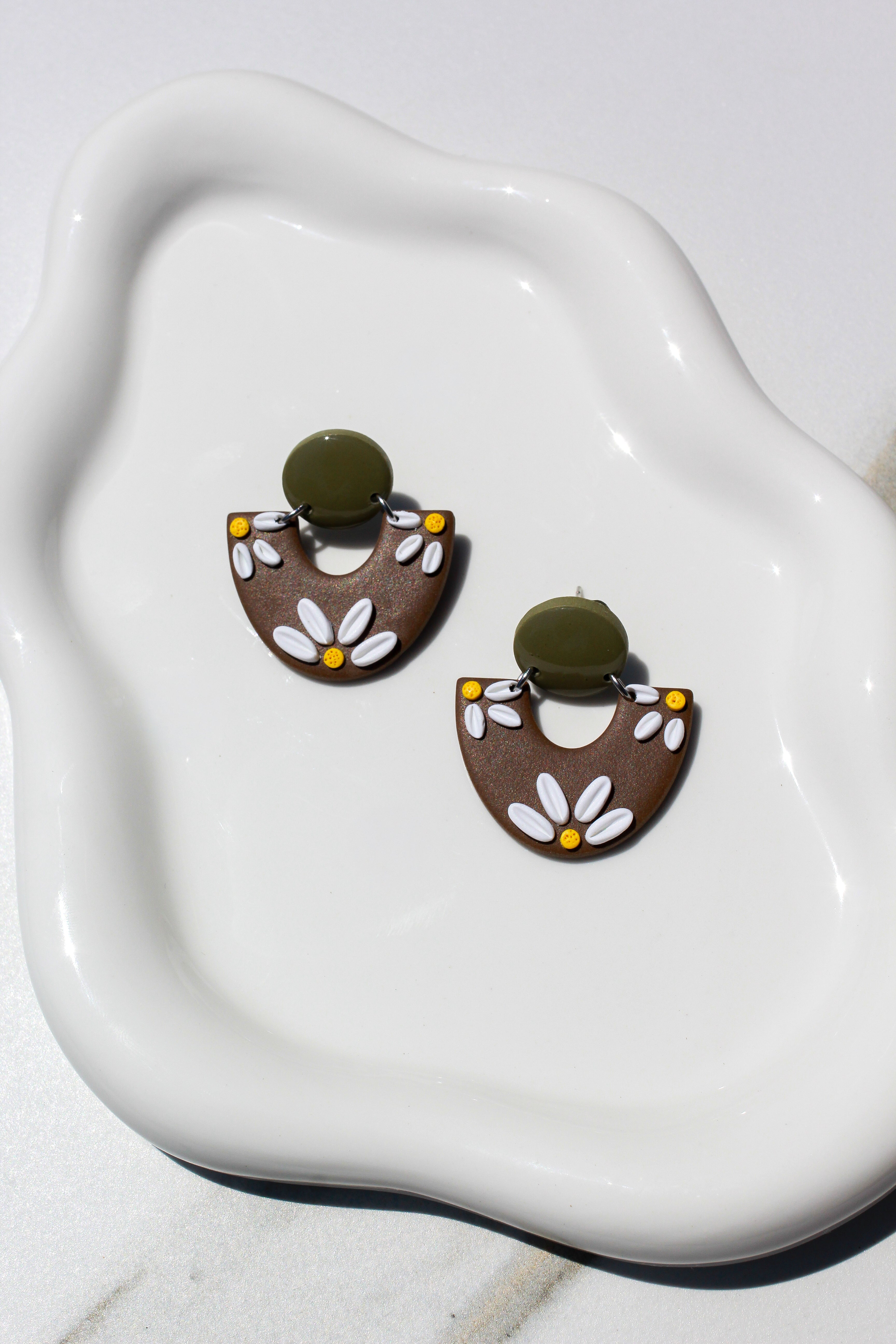 Pair of floral earrings on a white dish with a light background