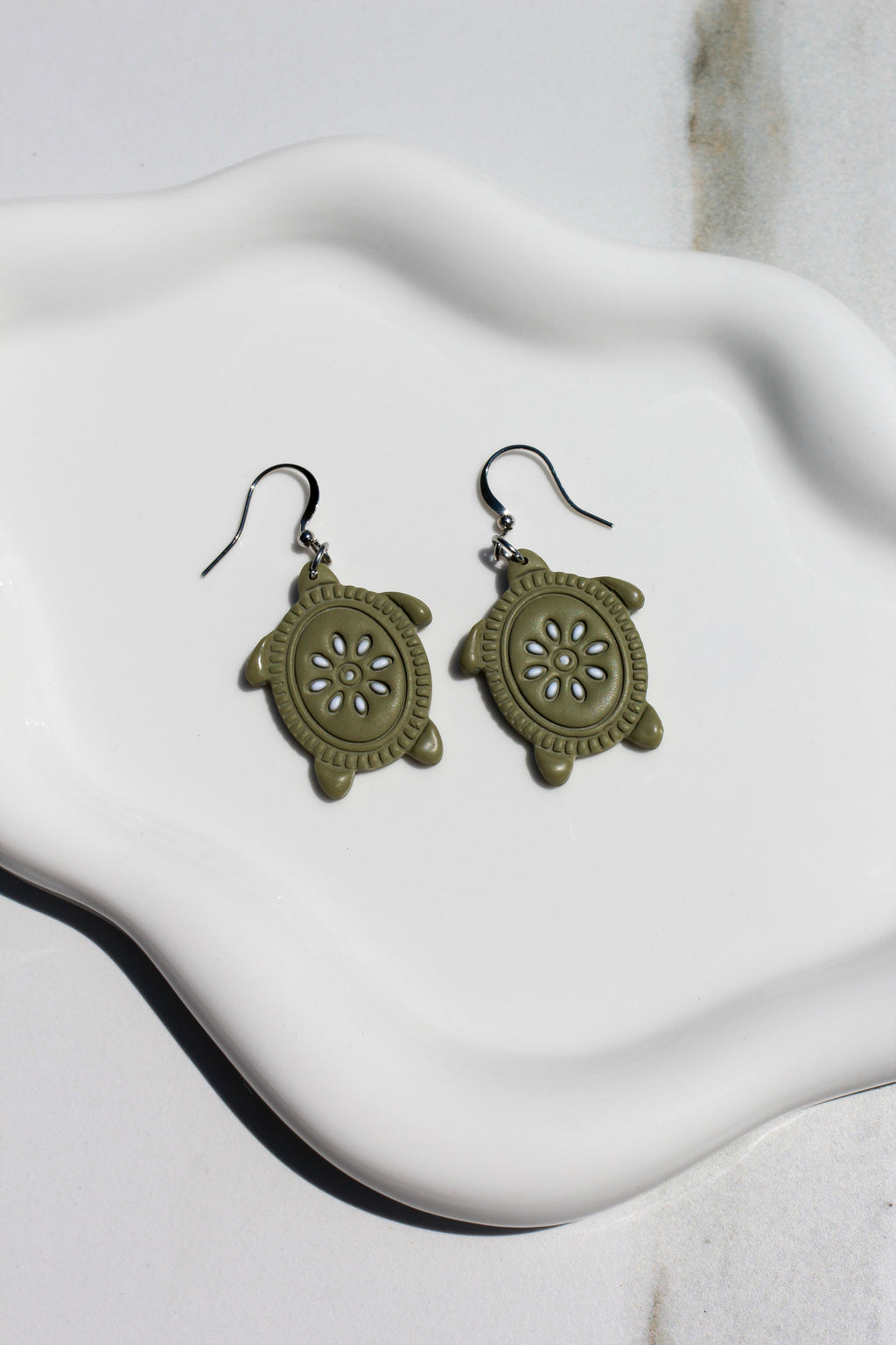 Pair of green turtle-shaped earrings on a white fabric background