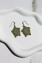 Pair of green turtle-shaped earrings on a white fabric background