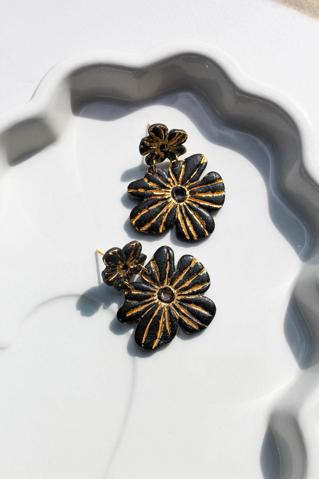 Black and gold floral earrings on a white dish