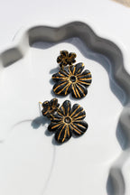 Black and gold floral earrings on a white dish