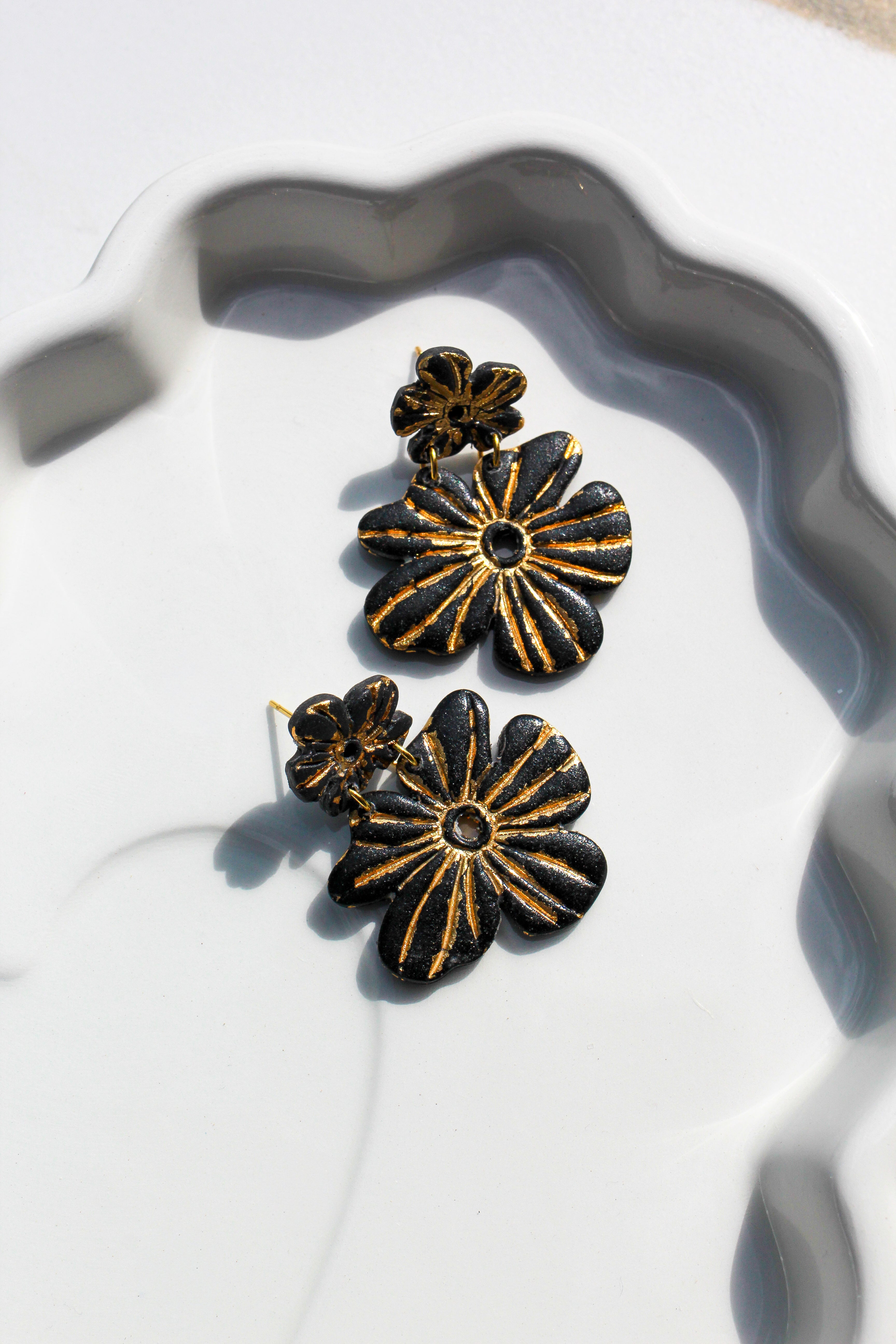Black and gold floral earrings on a white dish