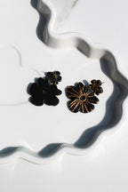 Pair of black and gold flower-shaped earrings on a white surface with wavy patterns.