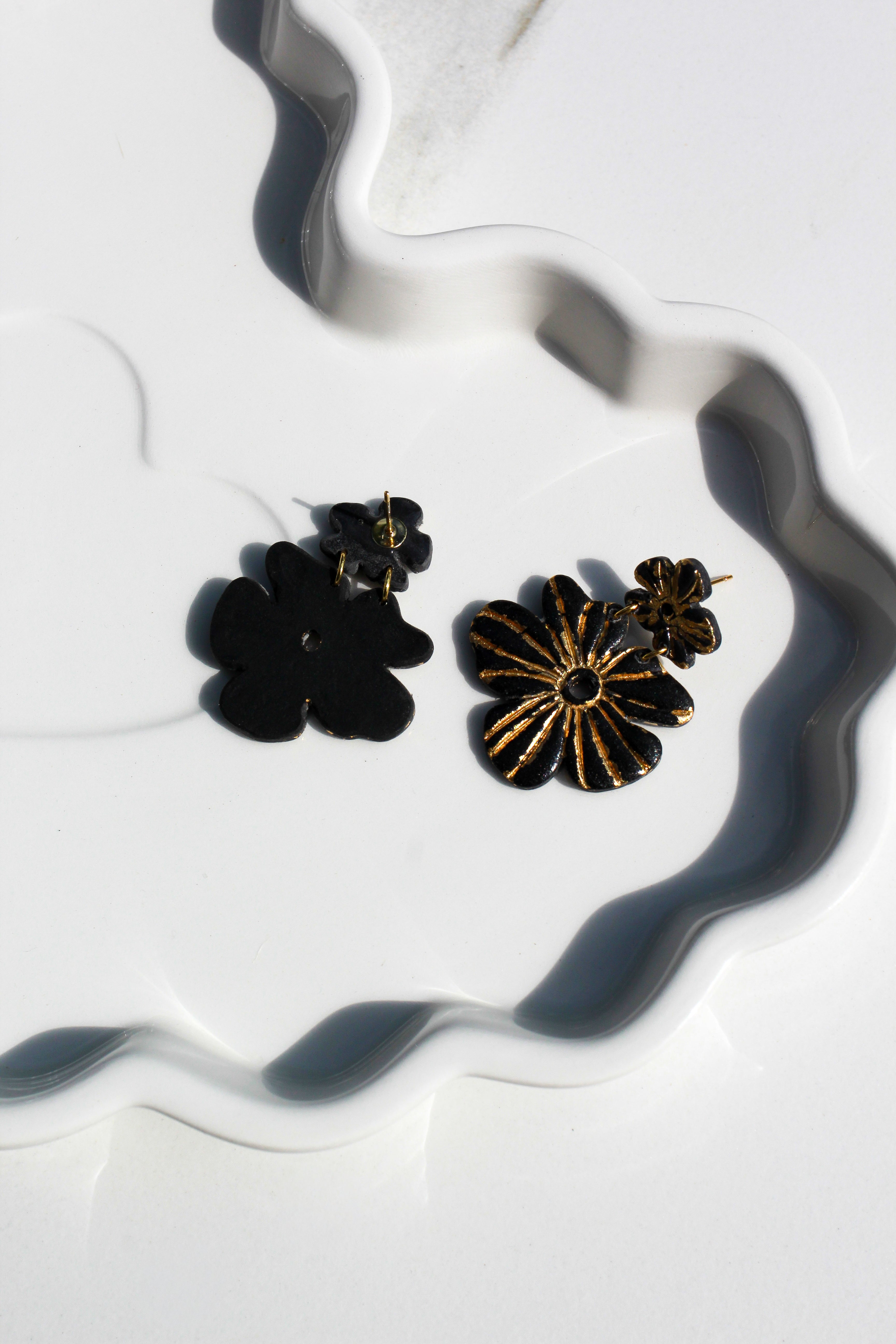 Pair of black and gold flower-shaped earrings on a white surface with wavy patterns.