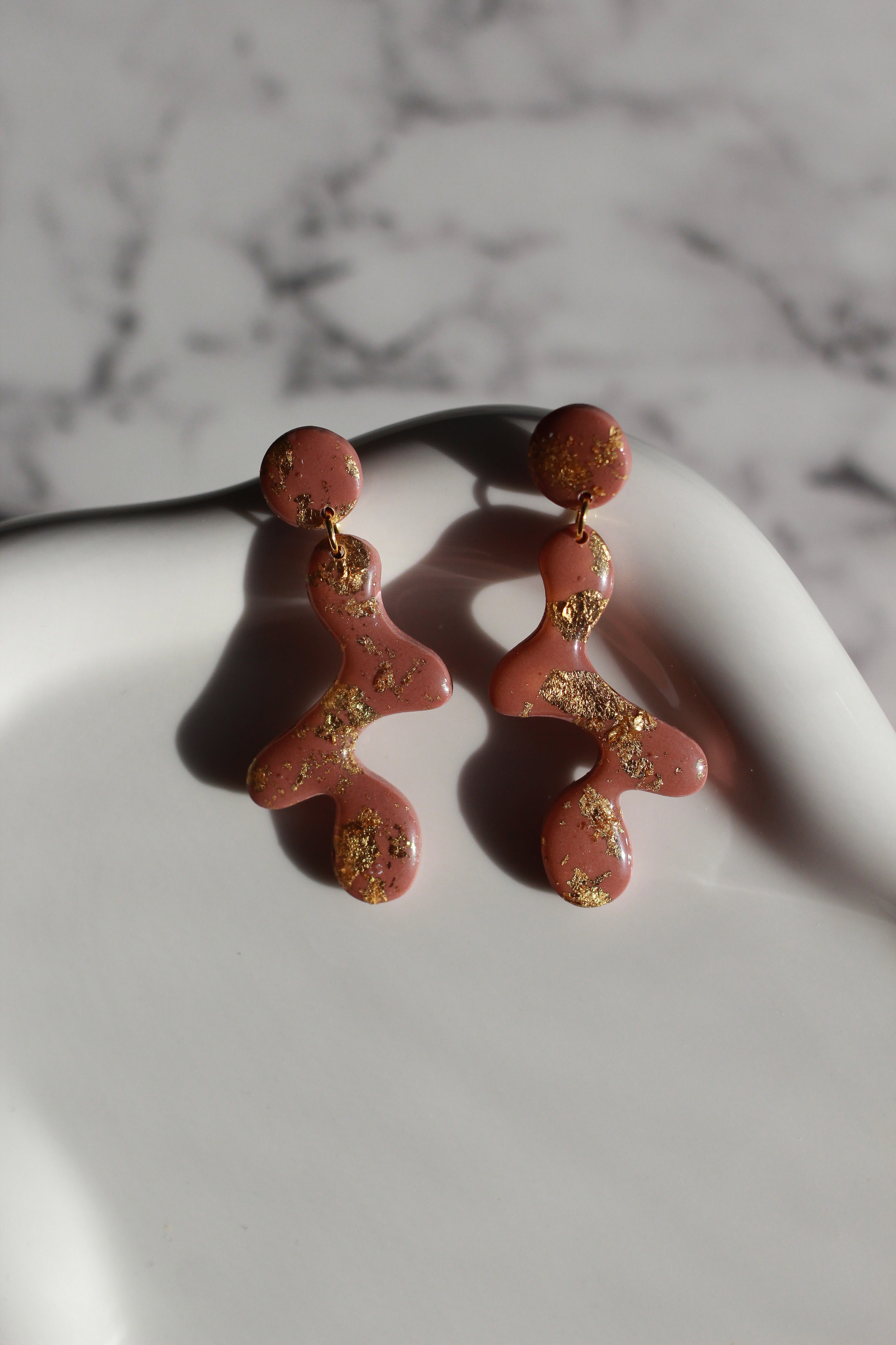 Mauve earrings with gold accents on a marble surface
