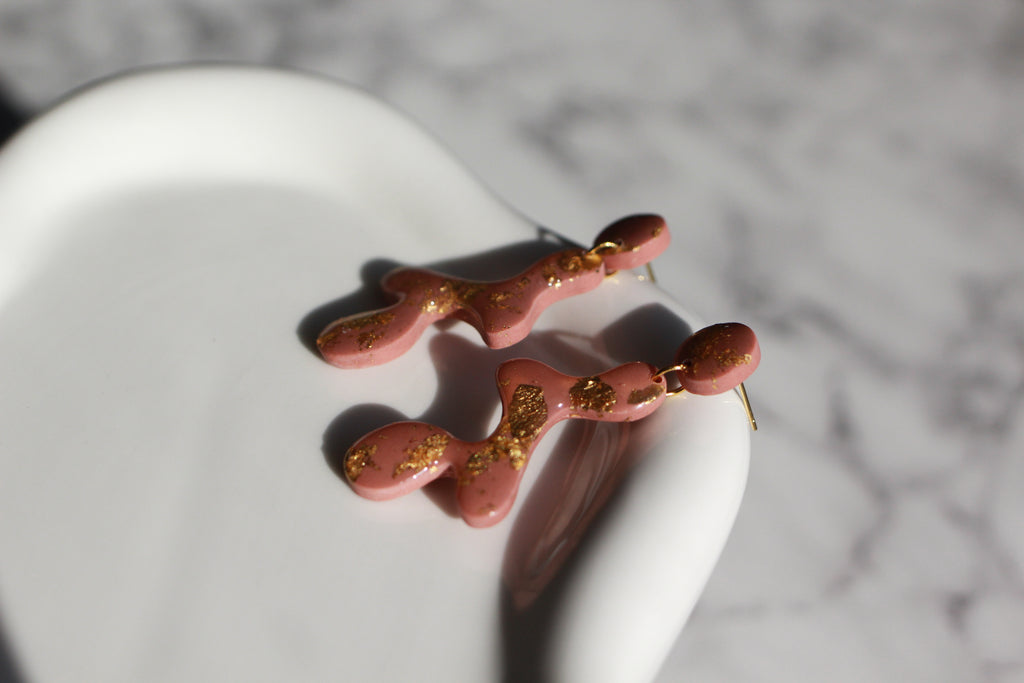 Mauve earrings with gold accents on a white surface