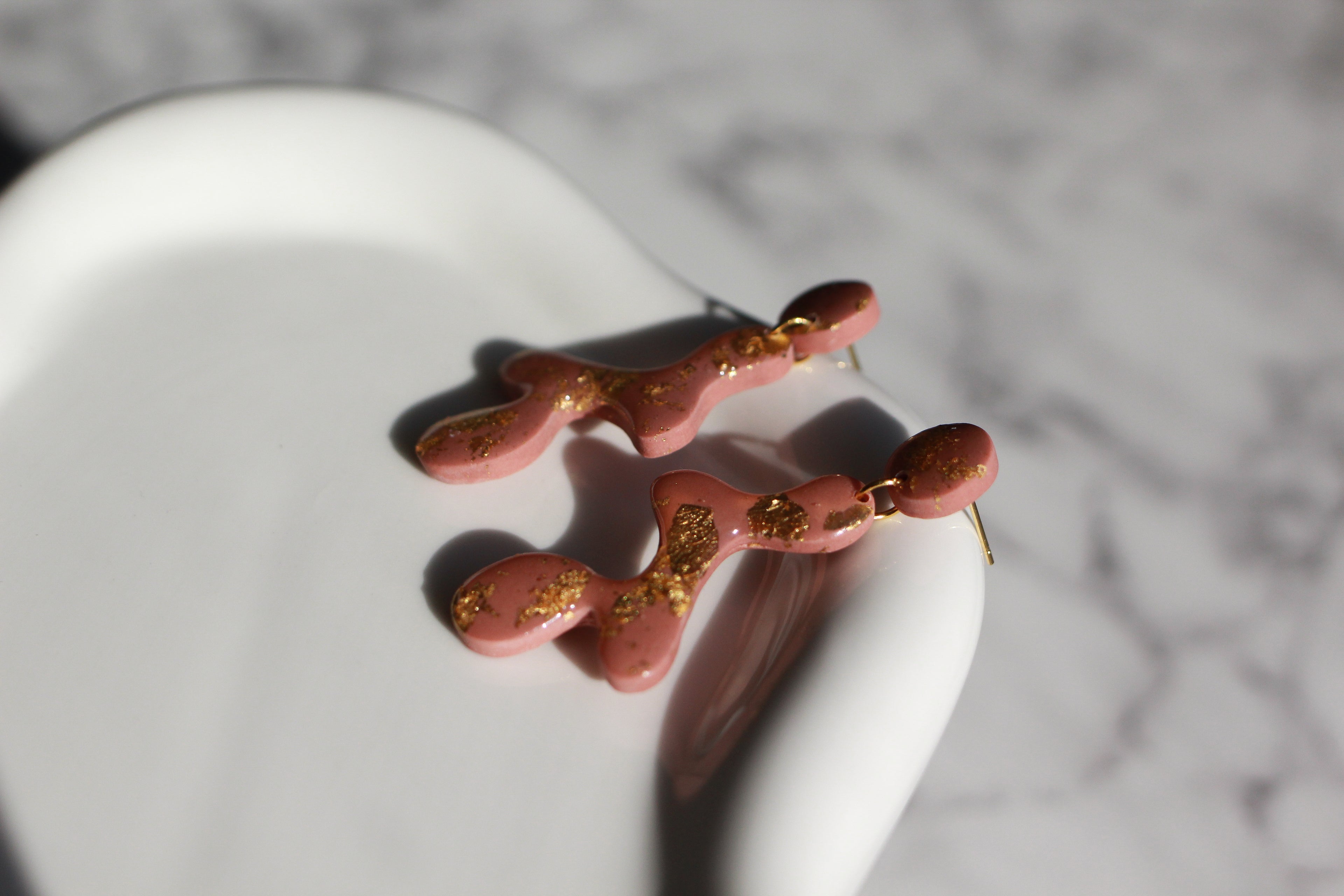 Mauve earrings with gold accents on a white surface