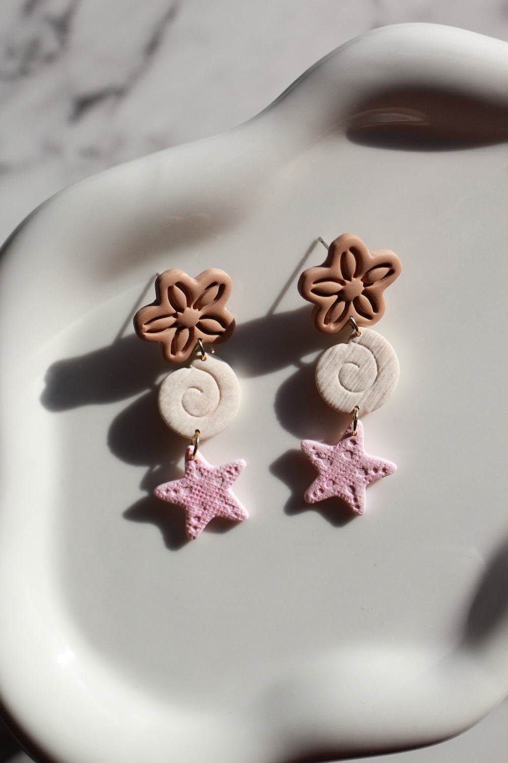 Pair of earrings with beachy floral and star designs on a marble surface
