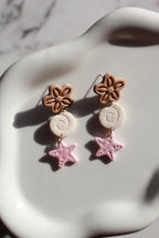 Pair of earrings with beachy floral and star designs on a marble surface