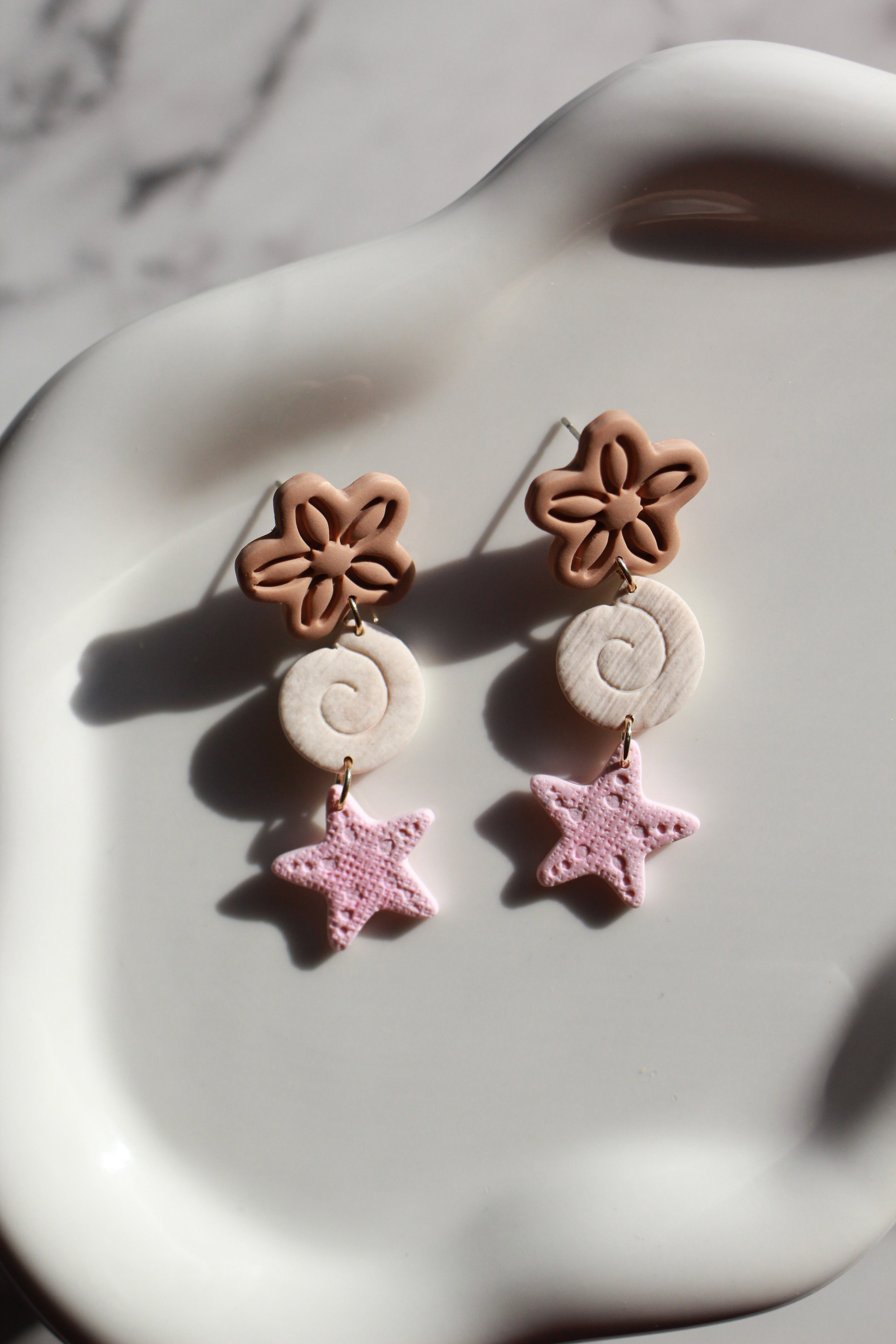 Pair of earrings with beachy floral and star designs on a marble surface