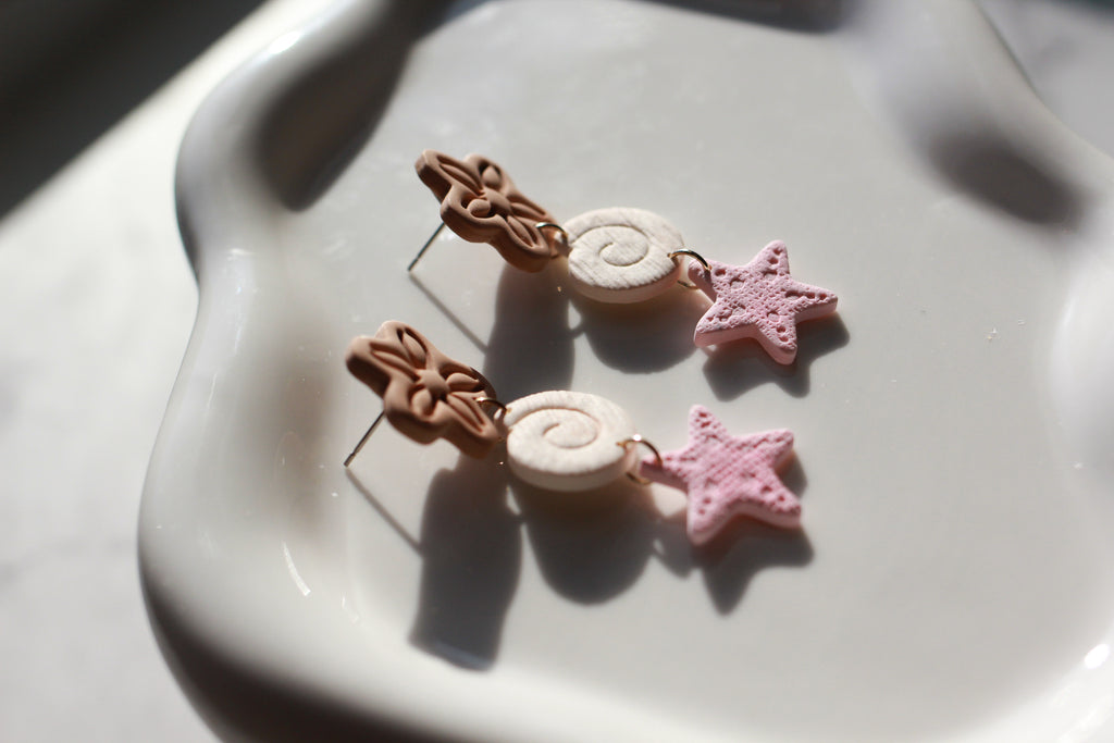 Pair of earrings with beachy floral and star designs on a marble surface