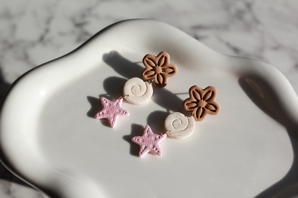 Pair of earrings with beachy floral and star designs on a marble surface