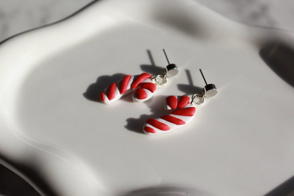Red and white candy cane-shaped earrings on a light gray surface