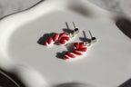 Red and white candy cane-shaped earrings on a light gray surface