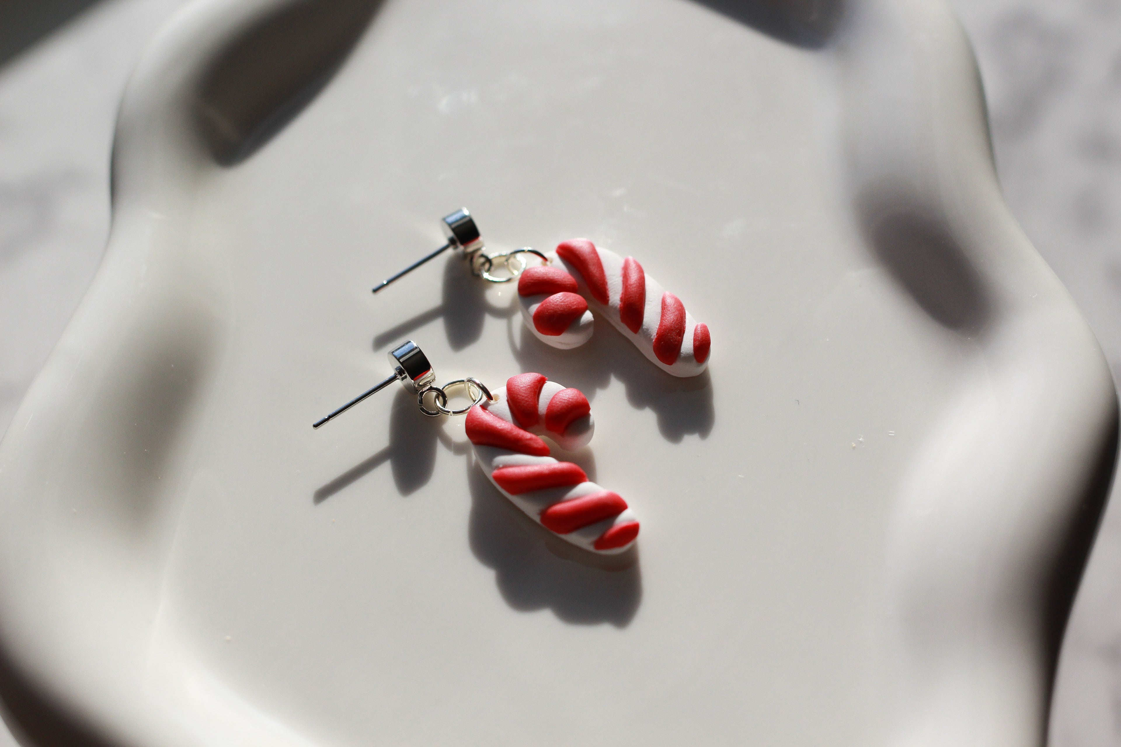 Candy cane-shaped earrings on a light gray surface