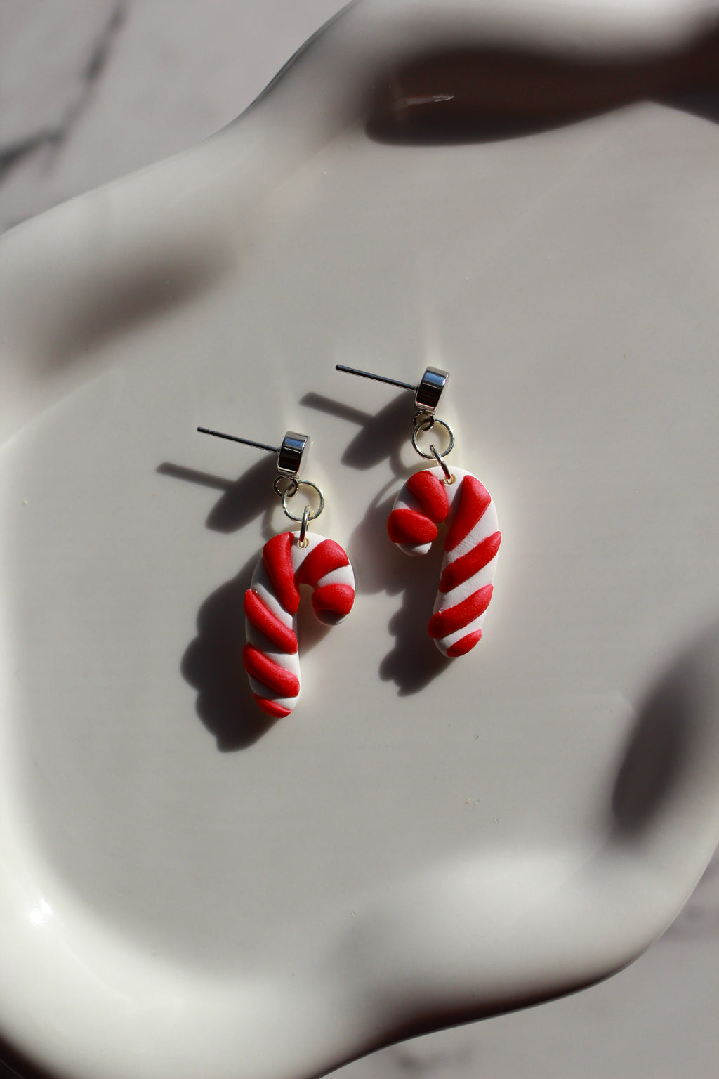 Red and white candy cane-shaped earrings on a white surface