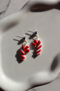 Red and white candy cane-shaped earrings on a white surface