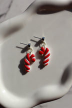 Red and white candy cane-shaped earrings on a white surface