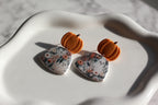 Earrings with pumpkin-shaped tops and floral-patterned fields with ghosts at the bottom on a white surface