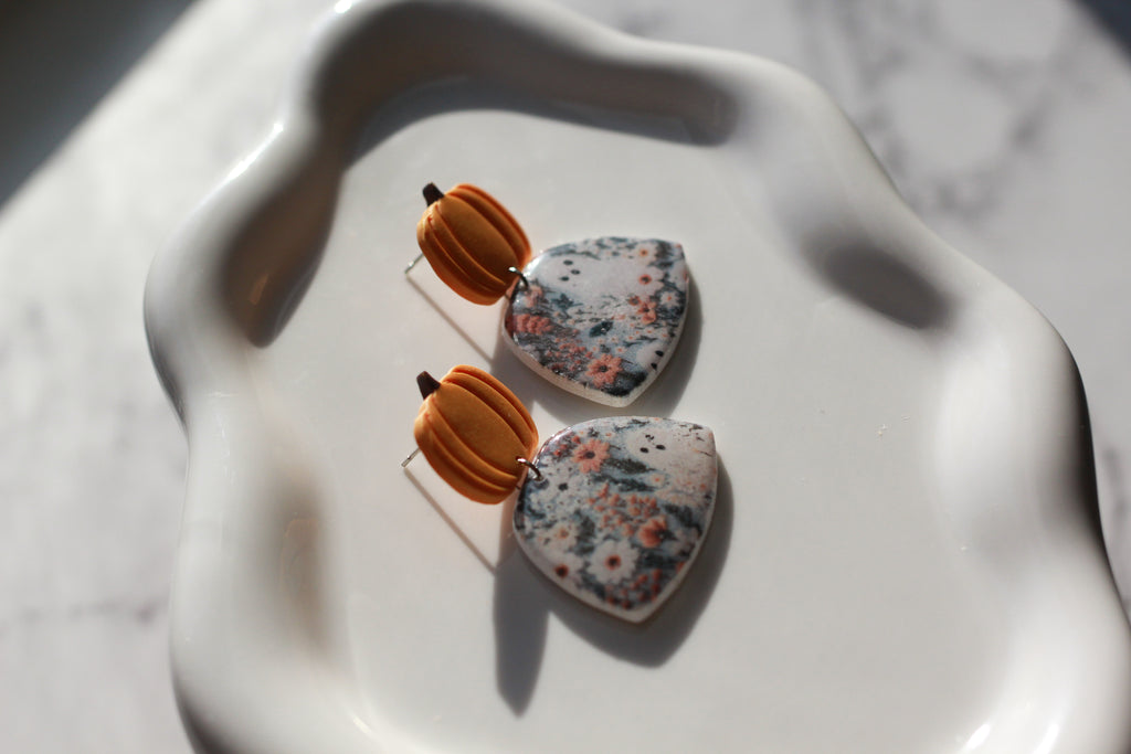 Earrings with pumpkin-shaped tops and floral-patterned fields with ghosts at the bottom on a white surface
