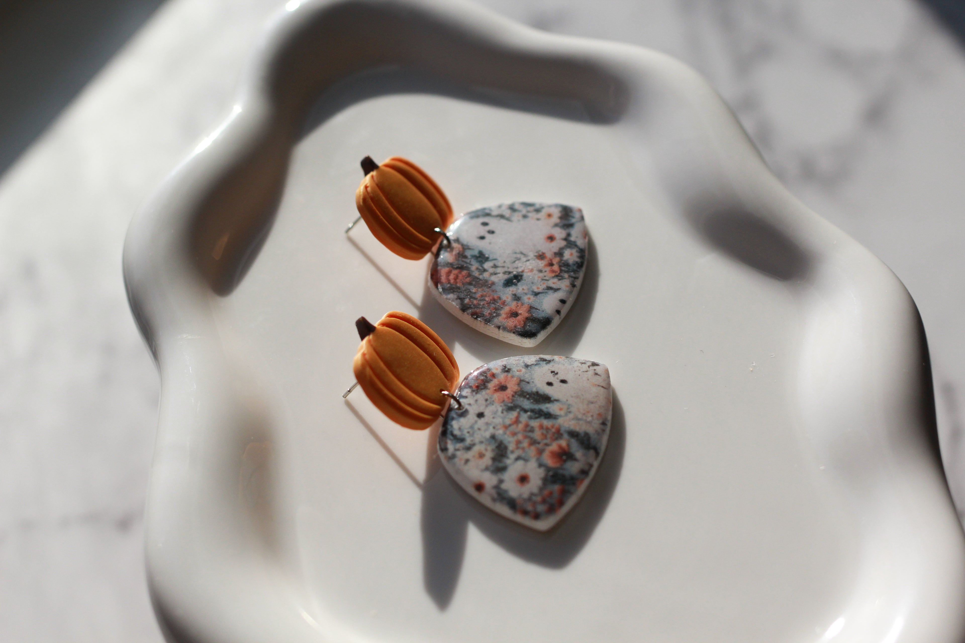 Earrings with pumpkin-shaped tops and floral-patterned fields with ghosts at the bottom on a white surface