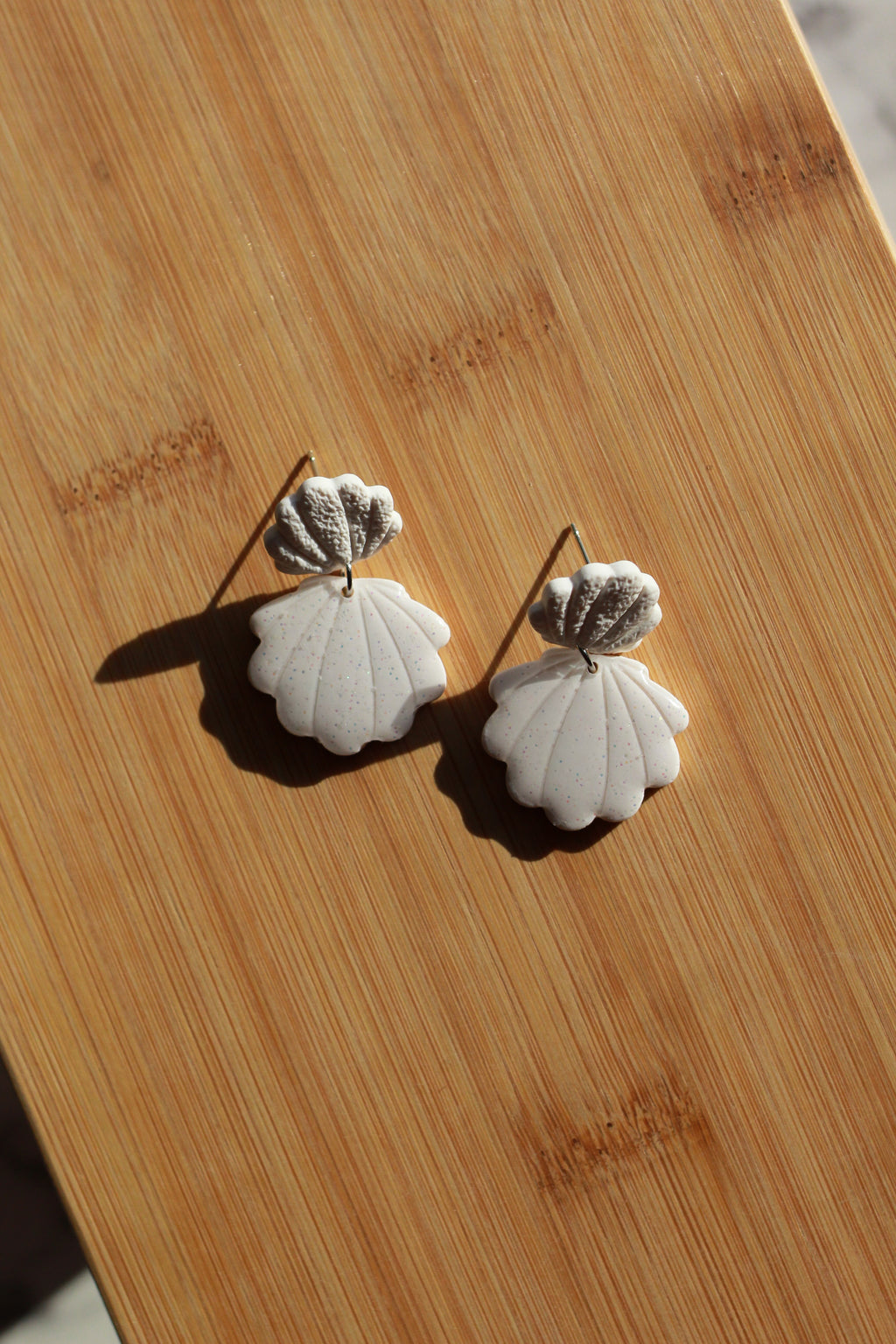 Pair of white shell-shaped earrings on a wooden surface
