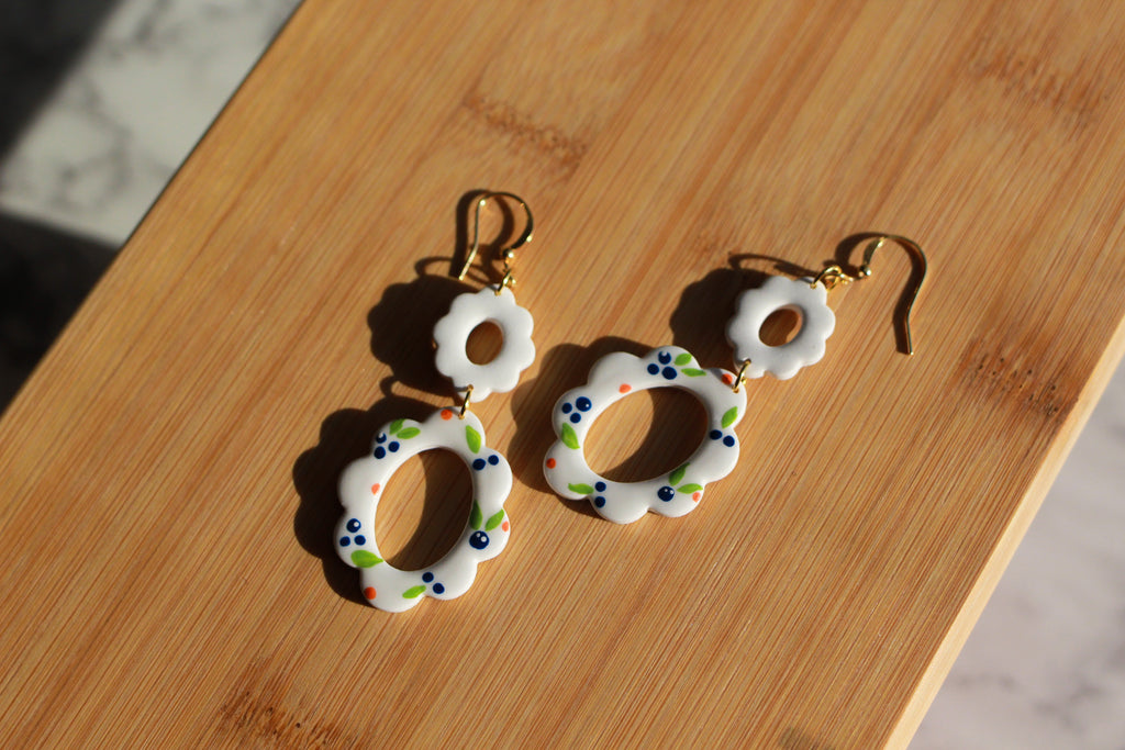 Pair of earrings with white circular designs on a wooden surface
