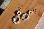 Pair of earrings with white circular designs on a wooden surface