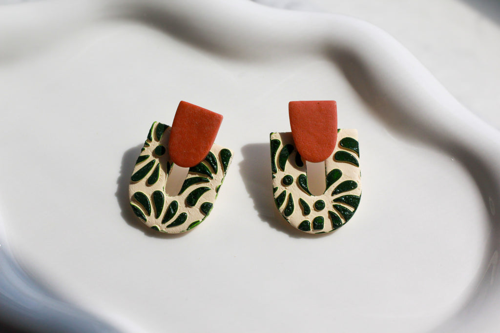 Pair of earrings with green leaf pattern and brown accents on a white fabric background