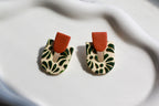 Pair of earrings with green leaf pattern and brown accents on a white fabric background