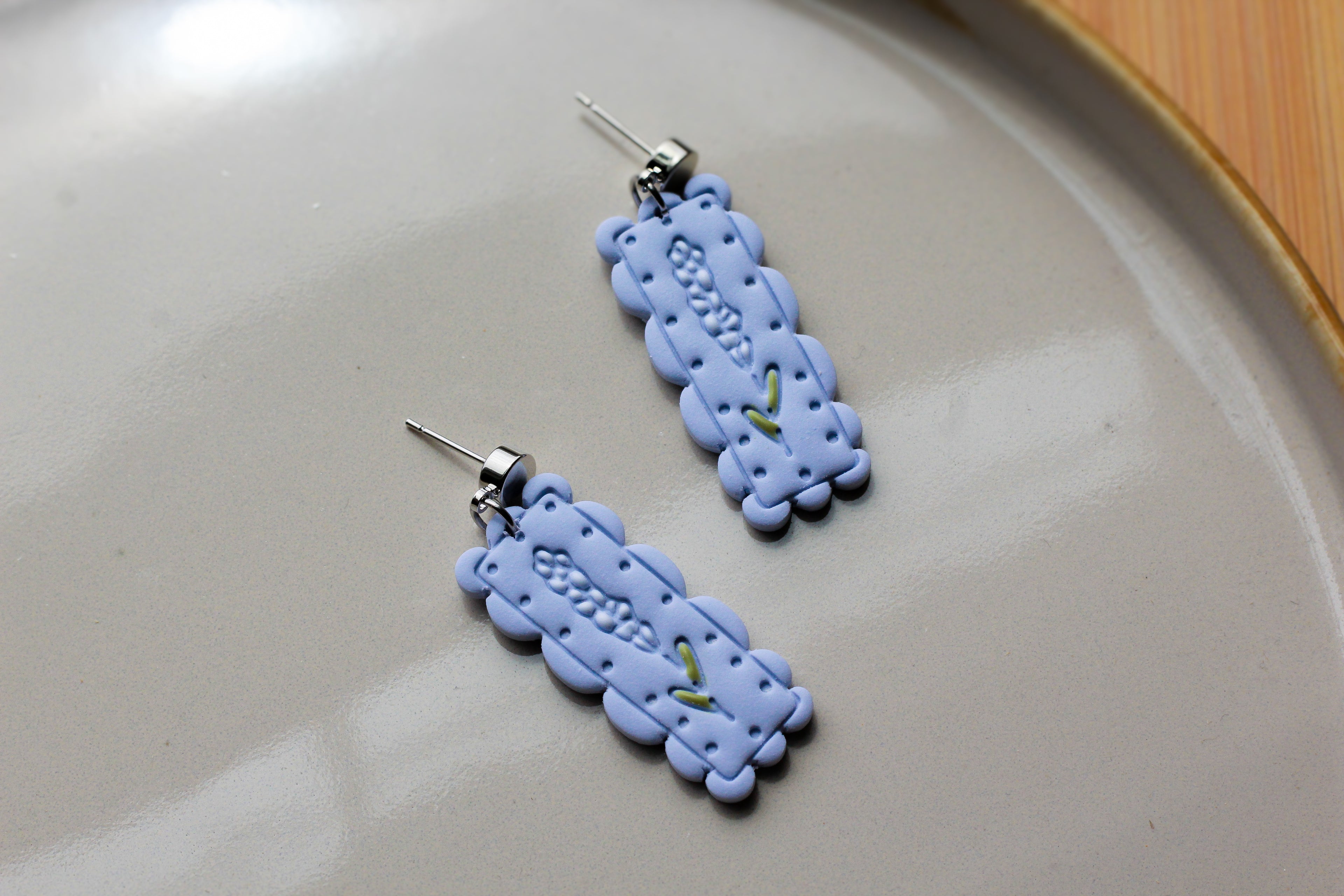 Pair of blue/purple lace-style earrings with white flowers on a light brown plate.