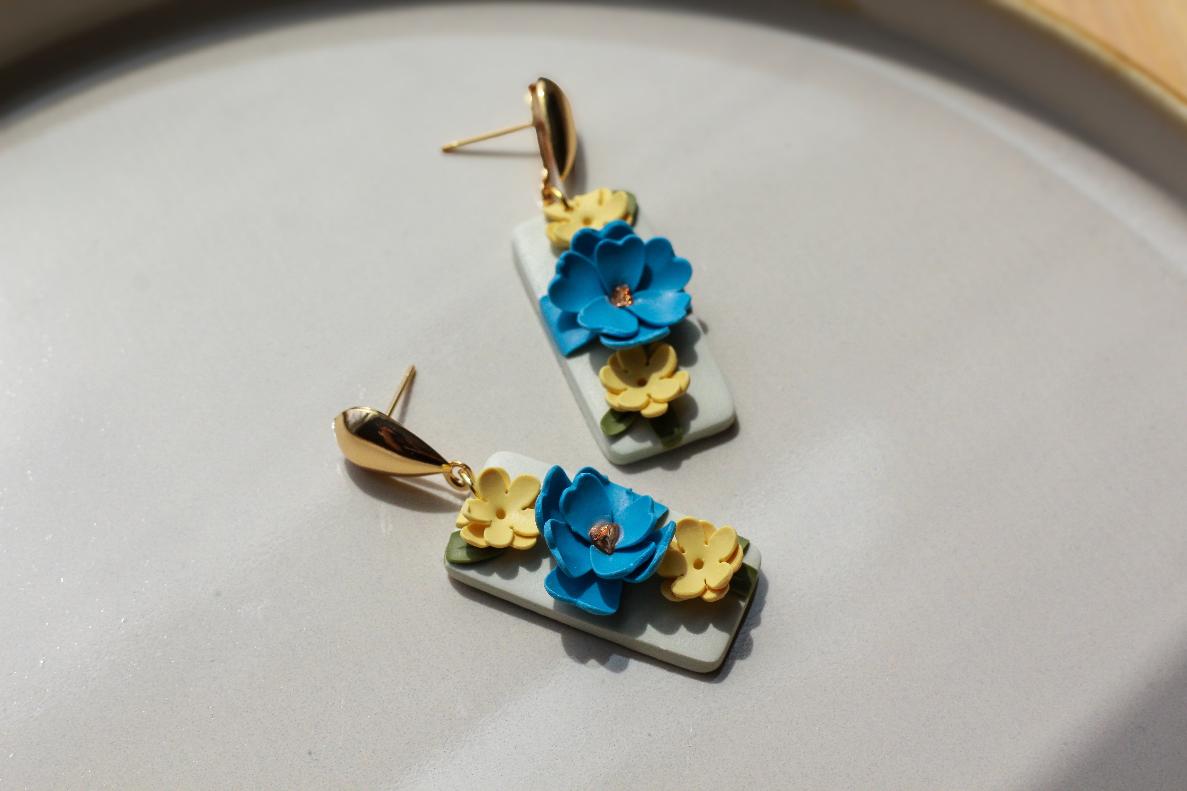 Floral earrings with blue and yellow flowers on a gray surface