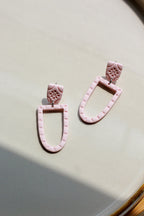 Pink earrings on a light beige surface