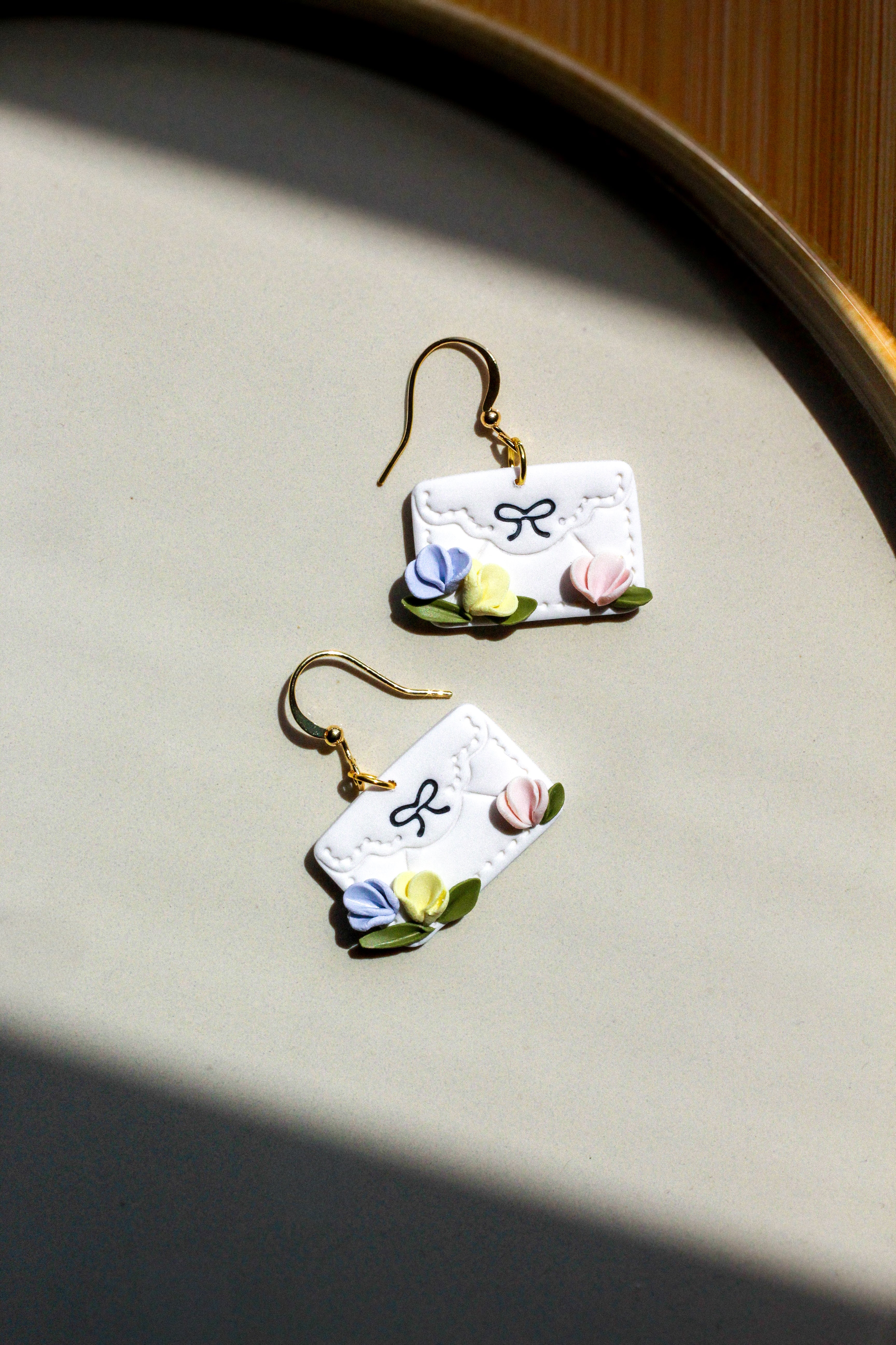Pair of envelope earrings with floral design on a neutral background