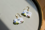 Pair of earrings shaped like white envelopes with floral designs on a light surface.