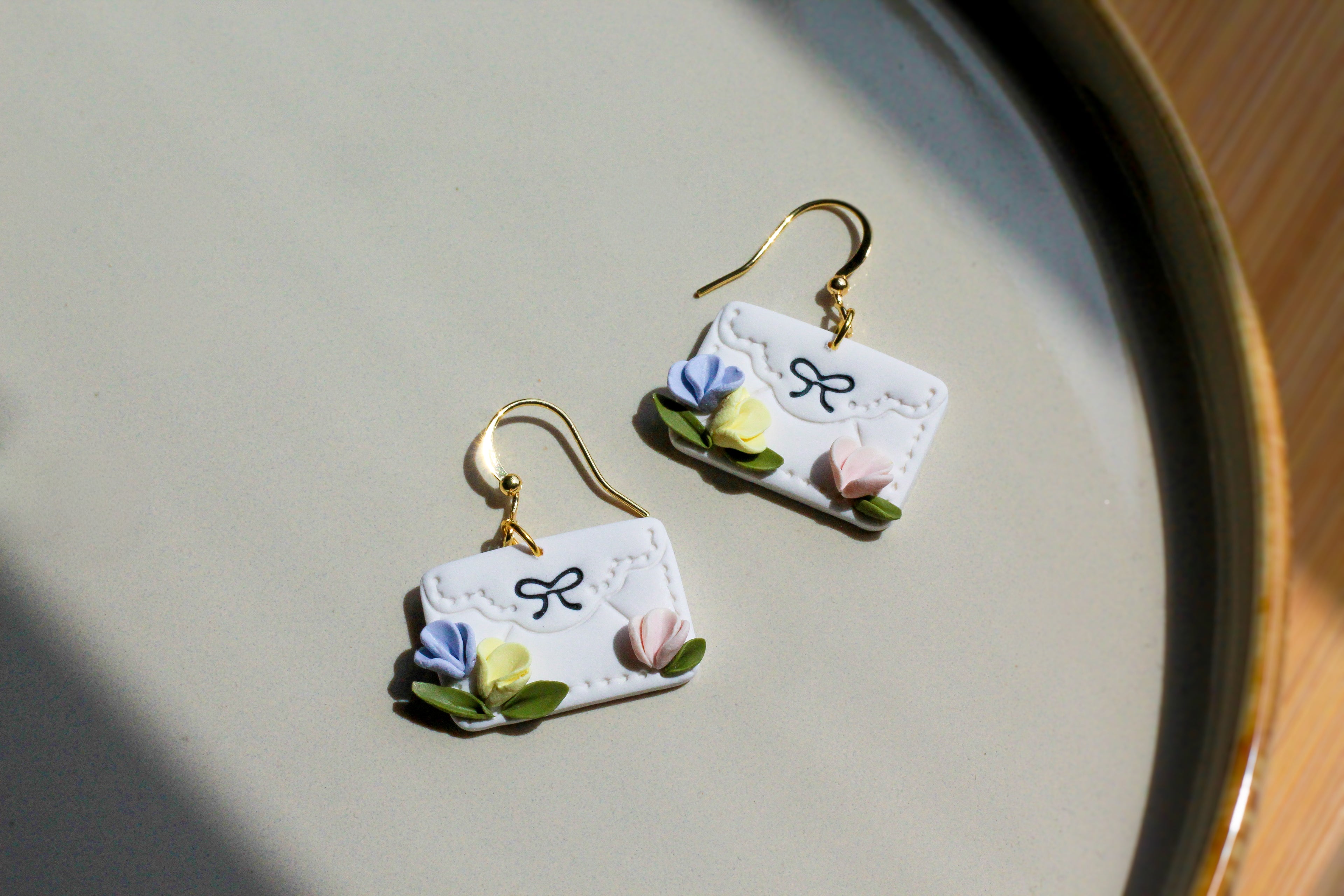 Pair of earrings shaped like white envelopes with floral designs on a light surface.