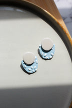Pair of blue and beige earrings on a light gray surface with a wooden edge.