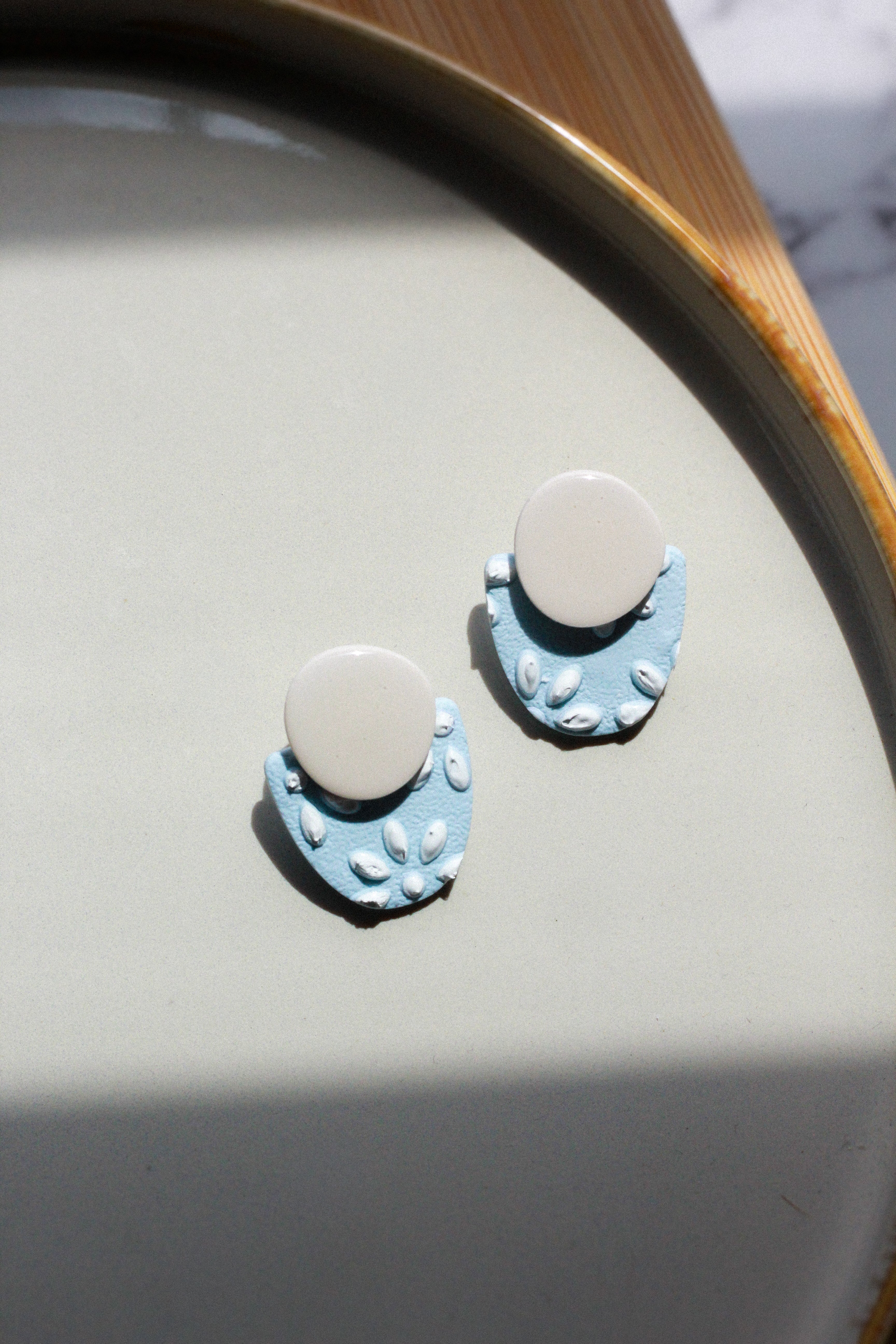 Pair of blue and beige earrings on a light gray surface with a wooden edge.